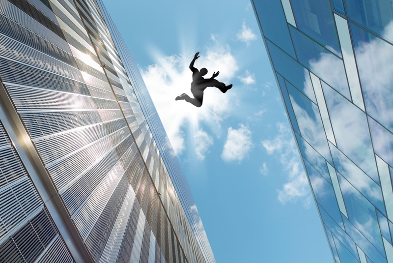 A man jumps from building to building with the sun reflected behind him